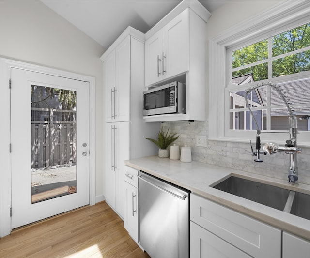 1015 Lincoln Ave, Ann Arbor, MI 48104 - kitchen featuring appliances with stainless steel finishes, backsplash, vaulted ceiling, a sink, and white cabinetry