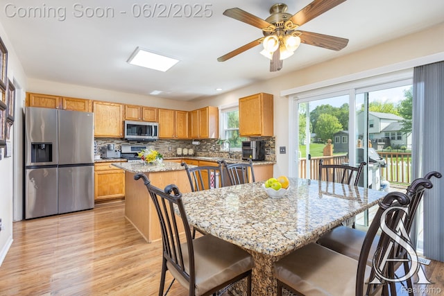6420 Crestview Dr, Holly, MI 48442 - kitchen with stainless steel appliances, a kitchen island, a kitchen breakfast bar, light wood finished floors, and tasteful backsplash