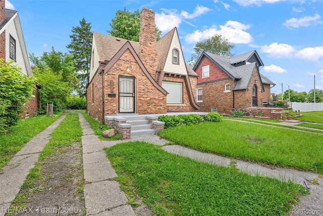 5935 Devonshire Rd, Dearborn, MI 48224 - english style home featuring brick siding, a chimney, a front yard, and a shingled roof