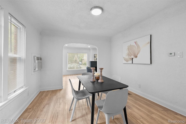 5935 Devonshire Rd, Dearborn, MI 48224 - dining area featuring a textured ceiling, arched walkways, light wood-style flooring, an AC wall unit, and baseboards
