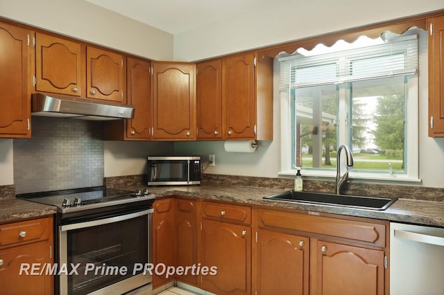 6461 Sheridan Rd, Saginaw, MI 48601 - kitchen with stainless steel appliances, under cabinet range hood, a sink, dark countertops, and brown cabinetry