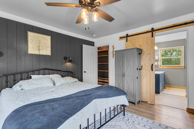 9410 US Highway 12, Brooklyn, MI 49230 - bedroom featuring a barn door, light wood-style flooring, baseboards, ceiling fan, and a walk in closet