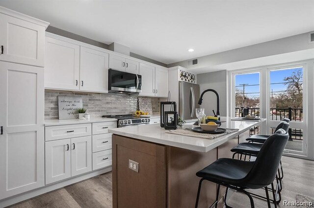 344 Main St Unit 300, Milford, MI 48381 - kitchen with appliances with stainless steel finishes, light wood-style flooring, a kitchen island with sink, white cabinetry, and backsplash