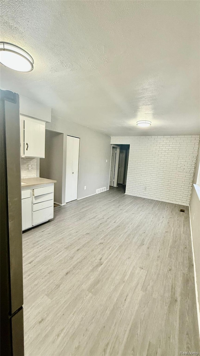 26304 Patricia Ave, Sterling Heights, MI 48091 - unfurnished living room with a textured ceiling, light wood-style flooring, baseboards, and brick wall