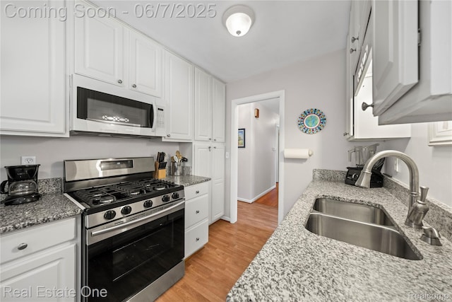 2253 Robell Dr, Commerce Twp, MI 48390 - kitchen with gas range, white microwave, a sink, white cabinetry, and light wood-style flooring