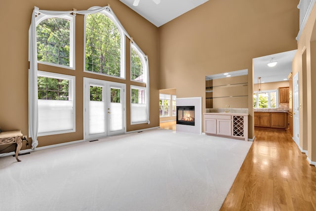 482 Torrington Dr W, Canton, MI 48188 - unfurnished living room featuring a towering ceiling, light wood finished floors, a glass covered fireplace, ceiling fan, and a sink