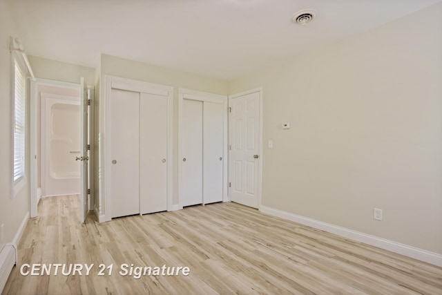 4769 S Fordney Rd, Hemlock, MI 48626 - unfurnished bedroom featuring two closets, light wood-style floors, baseboards, and a baseboard heating unit