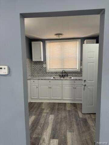 14557 Strathmoor St, Detroit, MI 48227 - kitchen featuring a sink, white cabinetry, dark wood-type flooring, and tasteful backsplash