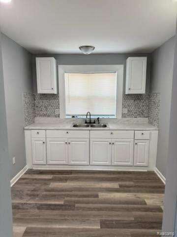 14557 Strathmoor St, Detroit, MI 48227 - kitchen featuring a sink, backsplash, and white cabinetry