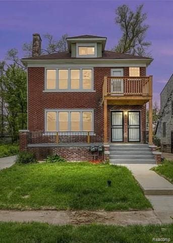 14557 Strathmoor St, Detroit, MI 48227 - back of property at dusk featuring a balcony, a chimney, brick siding, and a lawn
