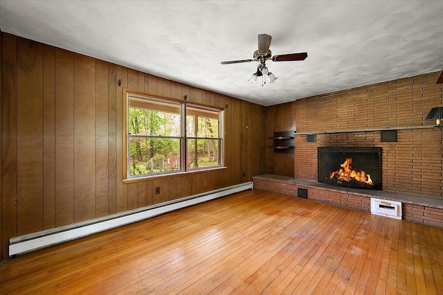 2100 Delhi W, Ann Arbor, MI 48103 - unfurnished living room with baseboard heating, hardwood / wood-style floors, a fireplace, ceiling fan, and wood walls