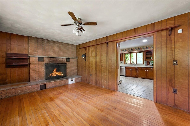 2100 Delhi W, Ann Arbor, MI 48103 - unfurnished living room featuring wooden walls, light wood-style floors, ceiling fan, a brick fireplace, and a sink