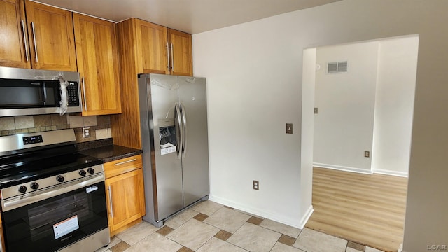 810 Division St, Adrian, MI 49221 - kitchen featuring stainless steel appliances, dark countertops, backsplash, brown cabinets, and baseboards