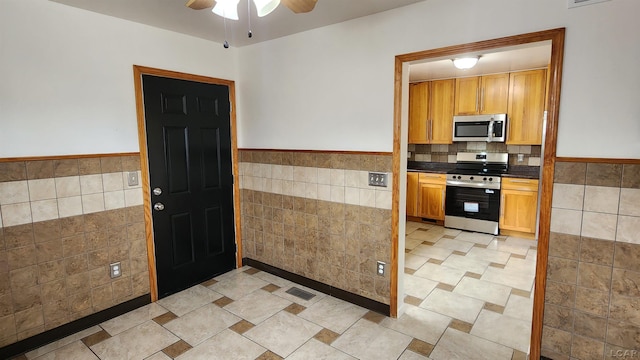810 Division St, Adrian, MI 49221 - kitchen featuring appliances with stainless steel finishes, tile walls, ceiling fan, a wainscoted wall, and dark countertops