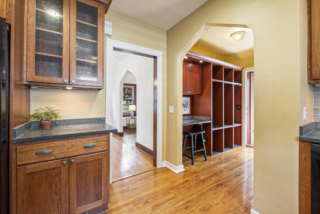 2323 Paris Ave SE, Grand Rapids, MI 49507 - kitchen featuring arched walkways, light wood-type flooring, dark countertops, glass insert cabinets, and brown cabinetry