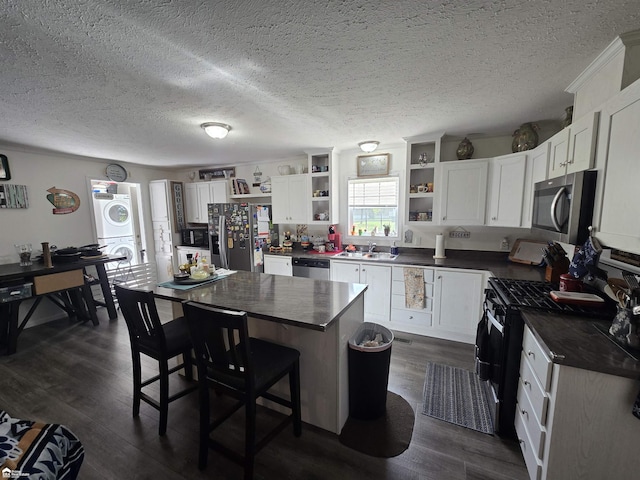 4101 S Sheridan Rd, Lennon, MI 48449 - kitchen with stainless steel appliances, open shelves, stacked washer / drying machine, dark countertops, and dark wood-type flooring
