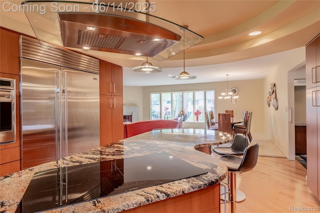 12950 Via Catherina Dr, Grand Blanc, MI 48439 - kitchen featuring appliances with stainless steel finishes, a kitchen bar, brown cabinetry, light wood-style floors, and stone countertops