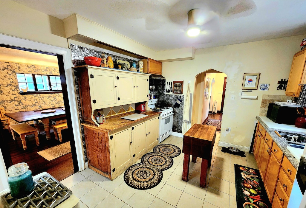 4489 Kensington Ave, Detroit, MI 48224 - kitchen with white range with gas stovetop, arched walkways, tasteful backsplash, a ceiling fan, and light countertops