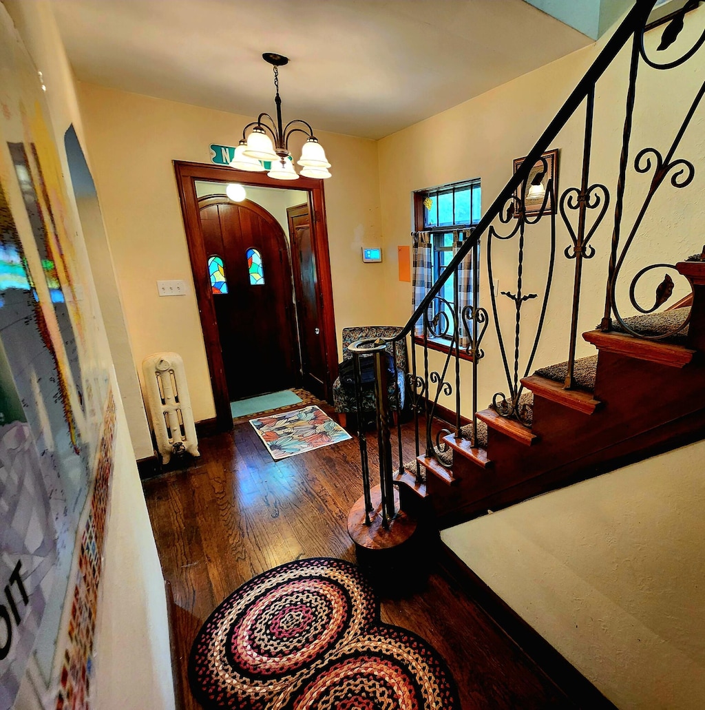 4489 Kensington Ave, Detroit, MI 48224 - entrance foyer with radiator, wood finished floors, arched walkways, stairway, and a chandelier