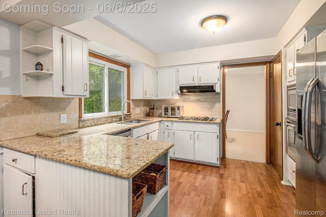 11187 Shadywood Dr, Brighton, MI 48114 - kitchen with open shelves, a sink, under cabinet range hood, a peninsula, and light stone countertops