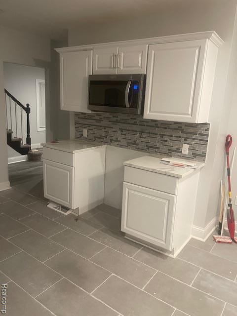 19961 Forrer St, Detroit, MI 48235 - kitchen featuring stainless steel microwave, light tile patterned floors, decorative backsplash, and white cabinets