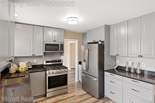 20605 Hickory St, Woodhaven, MI 48183 - kitchen featuring stainless steel appliances, light wood-style flooring, dark stone countertops, a sink, and gray cabinetry