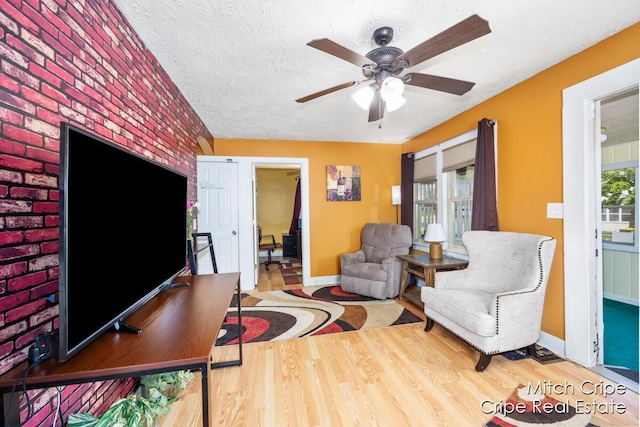772 26th St SW, Wyoming, MI 49509 - living area featuring wood finished floors, ceiling fan, baseboards, a textured ceiling, and brick wall