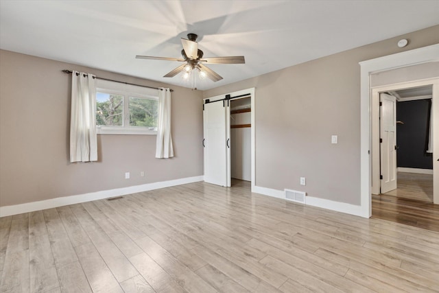 303 E Xy Ave, Vicksburg, MI 49097 - unfurnished bedroom featuring a barn door, light wood-style flooring, baseboards, and a ceiling fan