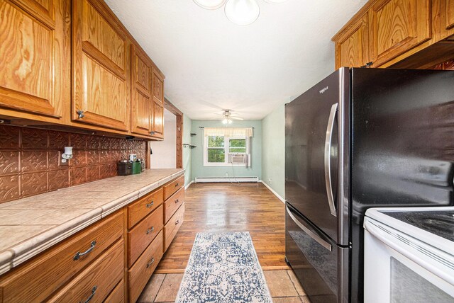 3225 Fishville Rd, Grass Lake, MI 49240 - kitchen featuring tile counters, tasteful backsplash, stove, freestanding refrigerator, and brown cabinetry