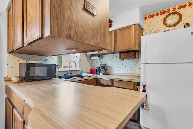 547 Pershing Ave, Jackson, MI 49203 - kitchen featuring freestanding refrigerator, black microwave, a sink, brown cabinetry, and wallpapered walls