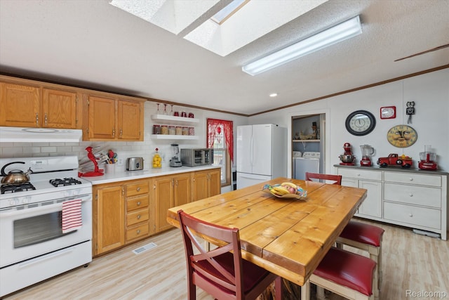 4952 Davison Rd, Lapeer, MI 48446 - kitchen with white appliances, under cabinet range hood, ornamental molding, washing machine and clothes dryer, and a skylight