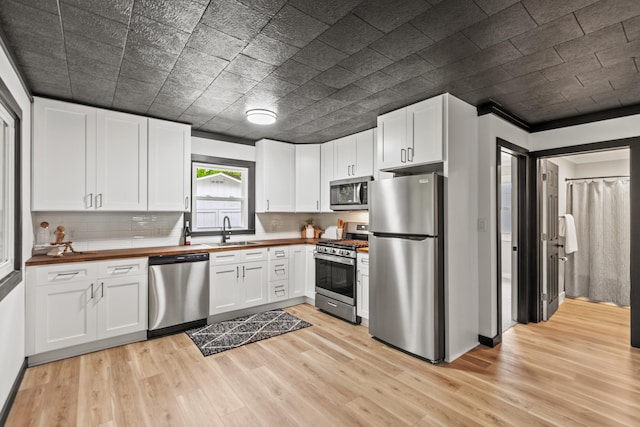 17465 Rapids Dr, Hersey, MI 49639 - kitchen featuring appliances with stainless steel finishes, a sink, light wood-style floors, white cabinets, and decorative backsplash