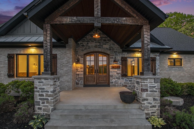 4035 136th Ave, Hamilton, MI 49419 - exterior entry at dusk with french doors, a standing seam roof, brick siding, a porch, and stone siding