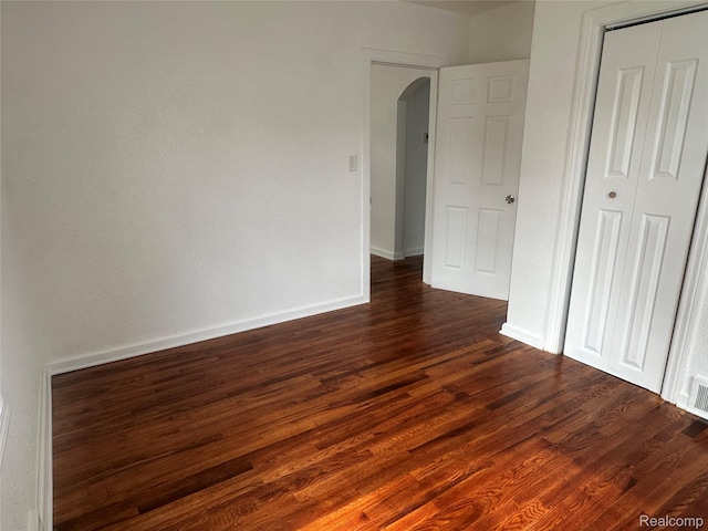 23767 Battelle Ave, Royal Oak, MI 48030 - unfurnished bedroom with arched walkways, dark wood-style flooring, baseboards, and a closet