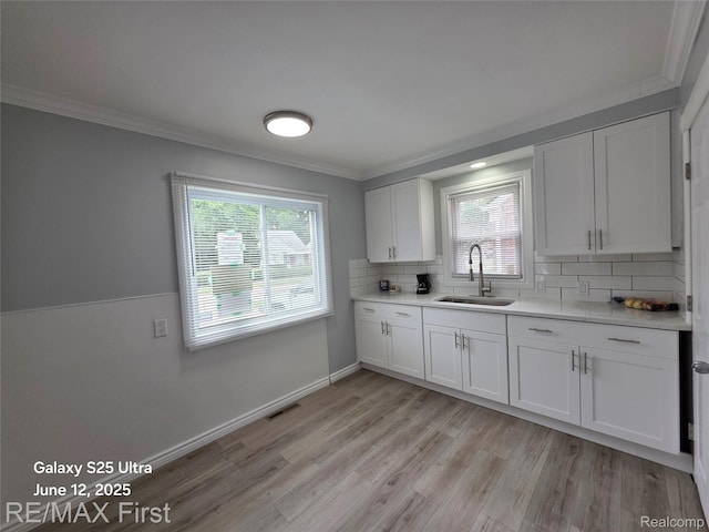 12725 Riverview St, Detroit, MI 48223 - kitchen featuring ornamental molding, light countertops, white cabinets, light wood finished floors, and tasteful backsplash