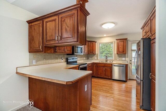 6063 Steeplechase Dr, Grand Blanc, MI 48439 - kitchen with stainless steel appliances, a sink, a peninsula, backsplash, and light wood finished floors