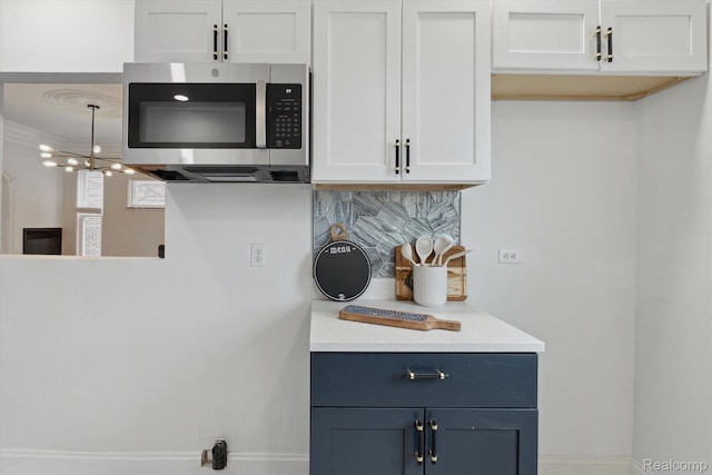 5784 Whittier St, Detroit, MI 48224 - kitchen with stainless steel microwave, light countertops, backsplash, white cabinetry, and a chandelier