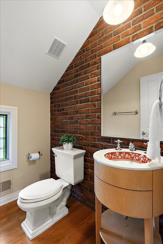 998 Eagle Ave, Ann Arbor, MI 48103 - bathroom with toilet, vaulted ceiling, brick wall, wood finished floors, and vanity
