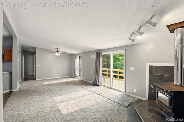 10900 Tuttlehill Rd, Milan, MI 48160 - unfurnished living room with a wood stove, a ceiling fan, a textured ceiling, baseboards, and track lighting