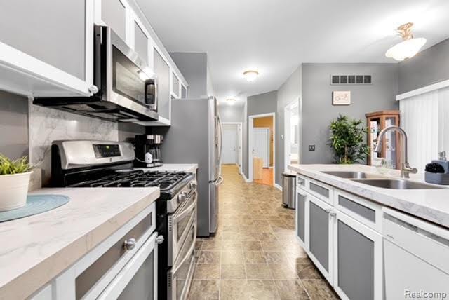 32051 W Cranston St, New Haven, MI 48048 - kitchen featuring stainless steel appliances, a sink, backsplash, white cabinetry, and glass insert cabinets
