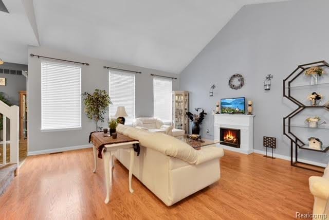 32051 W Cranston St, New Haven, MI 48048 - living area featuring light wood-style floors, a warm lit fireplace, high vaulted ceiling, and baseboards