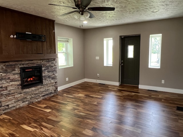 1302 Barnes St, Albion, MI 49224 - unfurnished living room featuring ceiling fan, a textured ceiling, a stone fireplace, baseboards, and dark wood-style floors