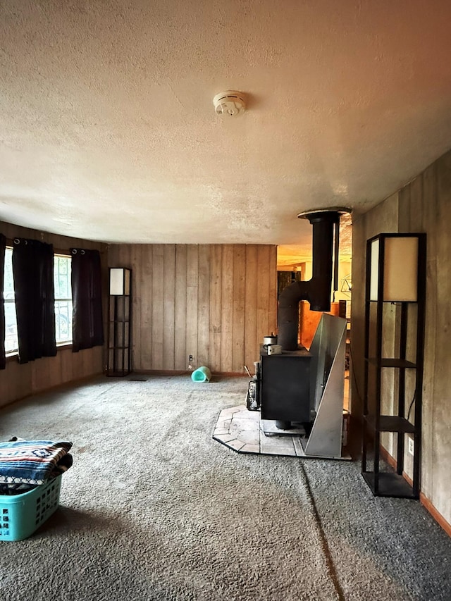 10750 16 Mile Rd NE, Cedar Springs, MI 49319 - unfurnished living room featuring a wood stove, carpet, a textured ceiling, and wood walls