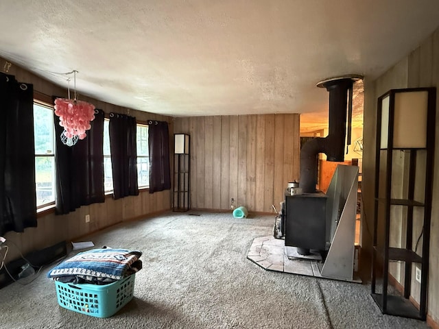 10750 16 Mile Rd NE, Cedar Springs, MI 49319 - unfurnished living room featuring a wood stove, carpet floors, wooden walls, a chandelier, and baseboards