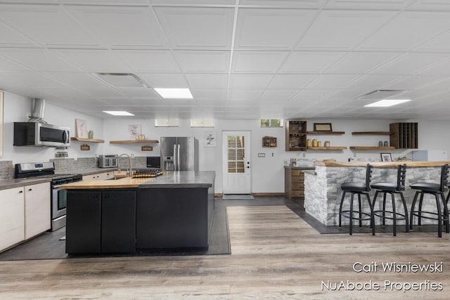 3732 E 128th St, Grant, MI 49327 - kitchen with appliances with stainless steel finishes, open shelves, a kitchen island with sink, and wood finished floors