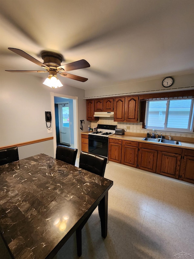 2285 Nebraska Ave, Saginaw, MI 48601 - kitchen with gas stove, under cabinet range hood, a sink, brown cabinets, and decorative backsplash