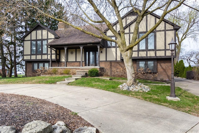 28220 Swan Island Dr, Grosse Ile, MI 48138 - tudor home with brick siding, a chimney, stucco siding, a front lawn, and covered porch
