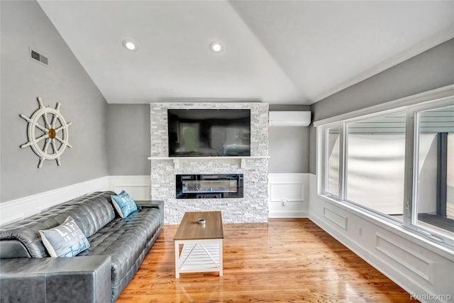 533 Bellevue Ave, Lake Orion, MI 48362 - living area featuring vaulted ceiling, a wainscoted wall, a stone fireplace, an AC wall unit, and wood finished floors