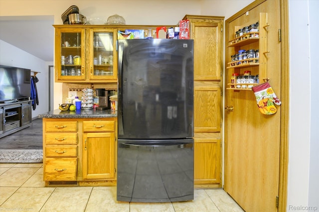 355 Carpenter Rd, Fostoria, MI 48435 - kitchen featuring freestanding refrigerator, light tile patterned floors, dark countertops, glass insert cabinets, and brown cabinets