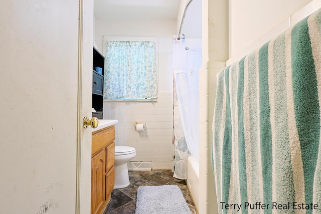 607 66th St SE, Grand Rapids, MI 49548 - bathroom with vanity, shower / bath combo with shower curtain, stone finish flooring, tile walls, and a wainscoted wall